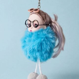 Hand holding a cute blue fluffy doll keychain with round glasses, pink bow, long light hair, and dangling pom-pom feet.