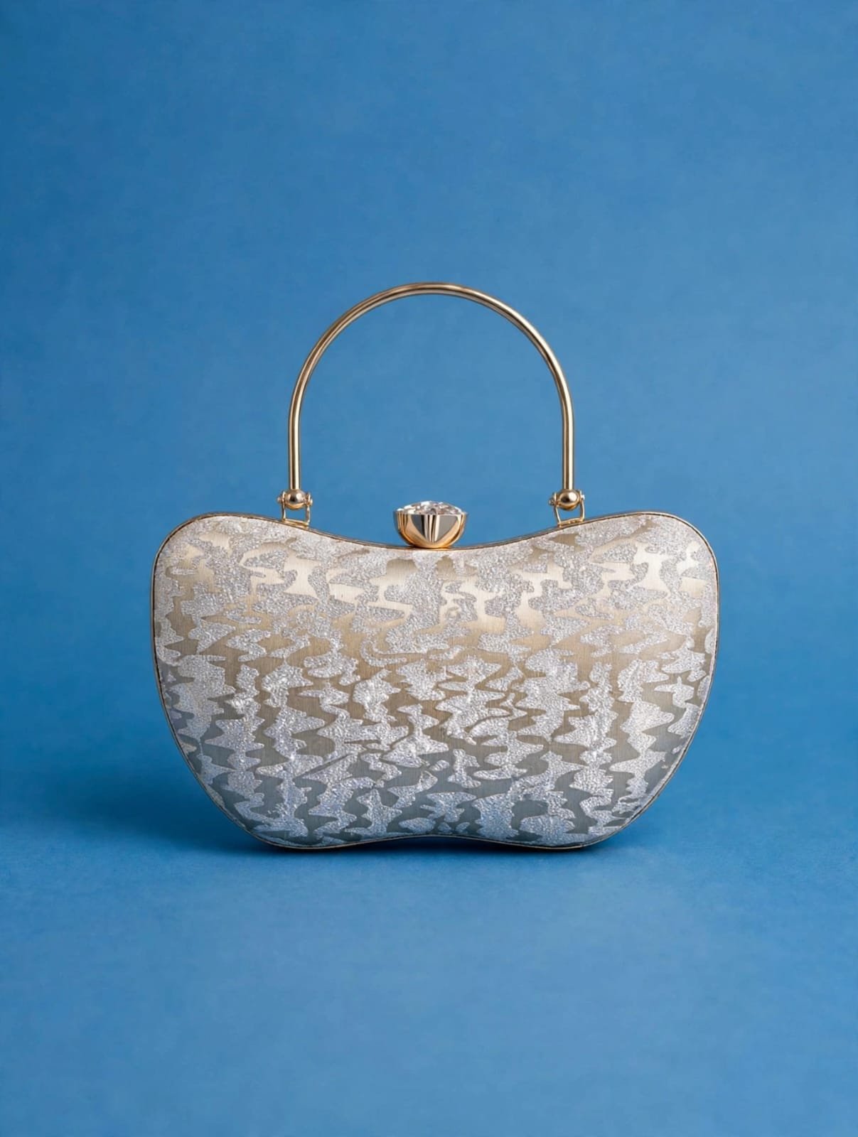 Silver glitter evening clutch with crystal clasp and gold metal top handle on a blue background