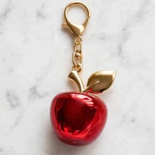 Glossy red apple keychain charm with gold leaf and lobster clasp on a white marble surface