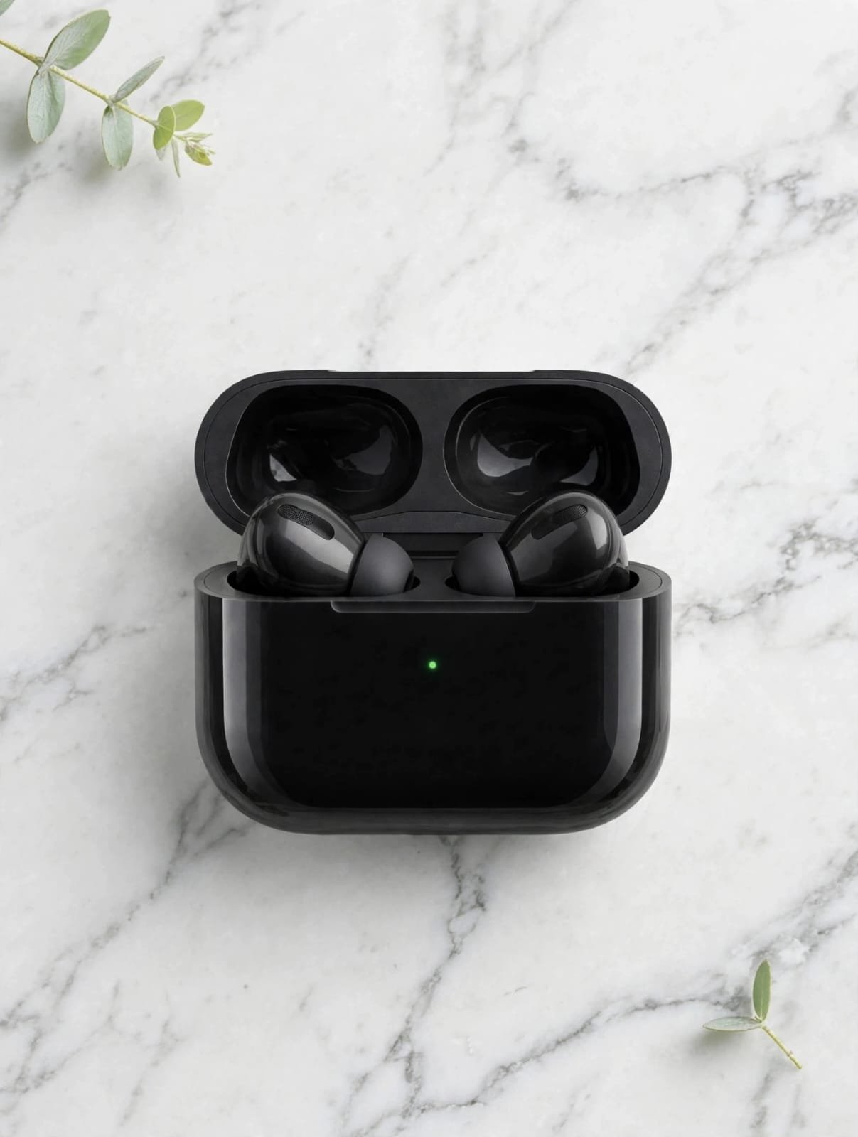 Black wireless earbuds in open glossy black charging case with green LED light on white marble background